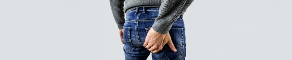 Sie sehen eine männliche Person, die Schmerzen im Anal-Bereich hat. Es könnte sich um eine Analfissur handeln. Eine Analfissur ist ein in vielen Fällen schmerzhafter Einriss der Haut oder Schleimhaut des Afters. Sie betrifft stereotyp die hintere Kommissur des Analkanals und verläuft radiär.