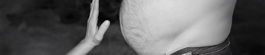 Sie sehen einen übergewichtigen Männerbauch. Übergewicht bei Männern (Adipositas bei Männern) Tatsächlich zeigen Studien, dass das Essverhalten von Männern sich deutlich von dem der Frauen unterscheidet. Während Frauen tendenziell kalorienbewusster essen und häufiger zu pflanzlichen Lebensmitteln greifen, bevorzugen Männer oft fettreiche, eiweißhaltige Kost – ein Verhalten, das evolutionsgeschichtlich geprägt ist. Doch diese Ernährungsgewohnheiten bergen gesundheitliche Risiken und begünstigen die Entstehung von Adipositas bei Männern.
