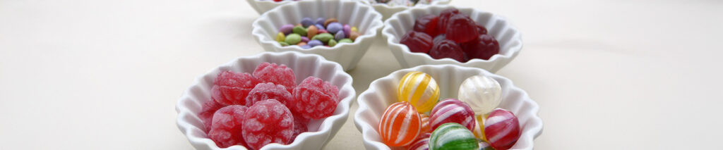 Sie sehen Bonbons in weißen Schalen. Das Bild steht für die Rubrik Karies.