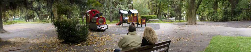Sie sehen ein kinderloses Pärchen die auf einer Bank auf einen Spielplatz schauen. Das Bild steht für die Rubrik Kinderlosigkeit.